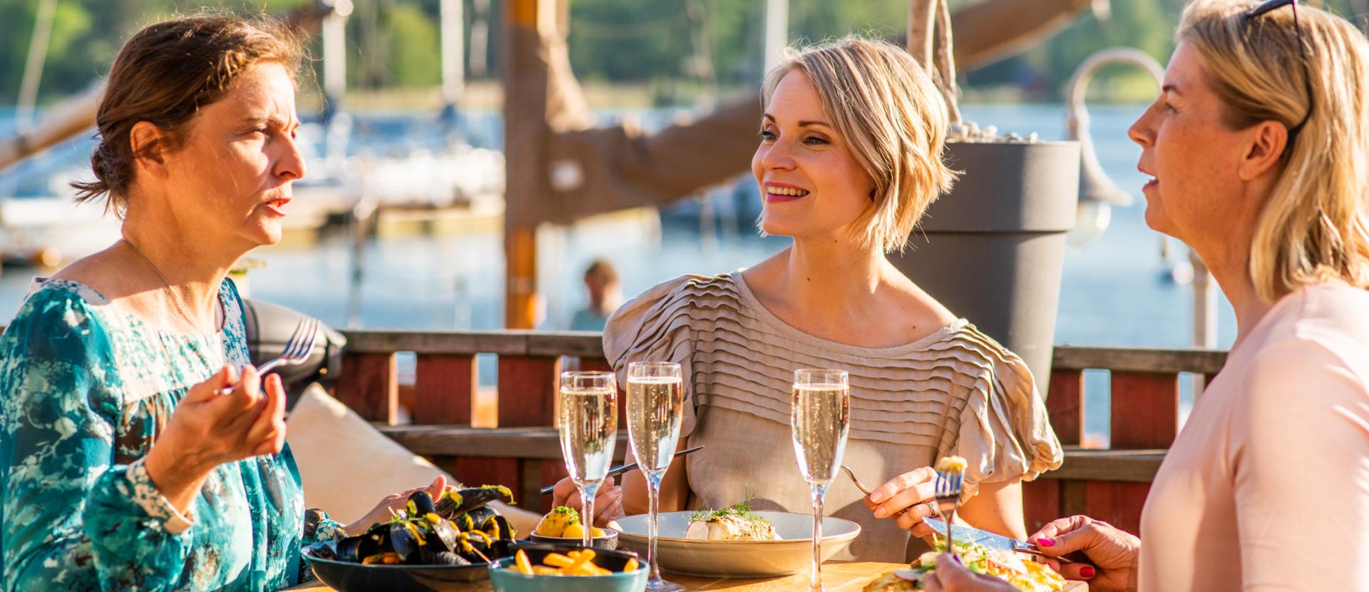 Tre kvinnor äter middag vid ÅSS Paviljongen vid vattnet i västra Mariehamn.